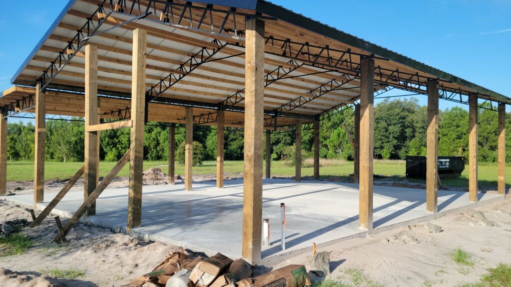 Construction site with a wooden framed carport, concrete base, and dark roof.