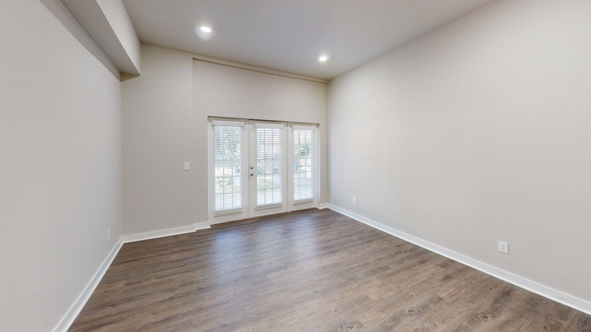 Empty modern room with gray walls, wood flooring, recessed lights, and French doors to a balcony.