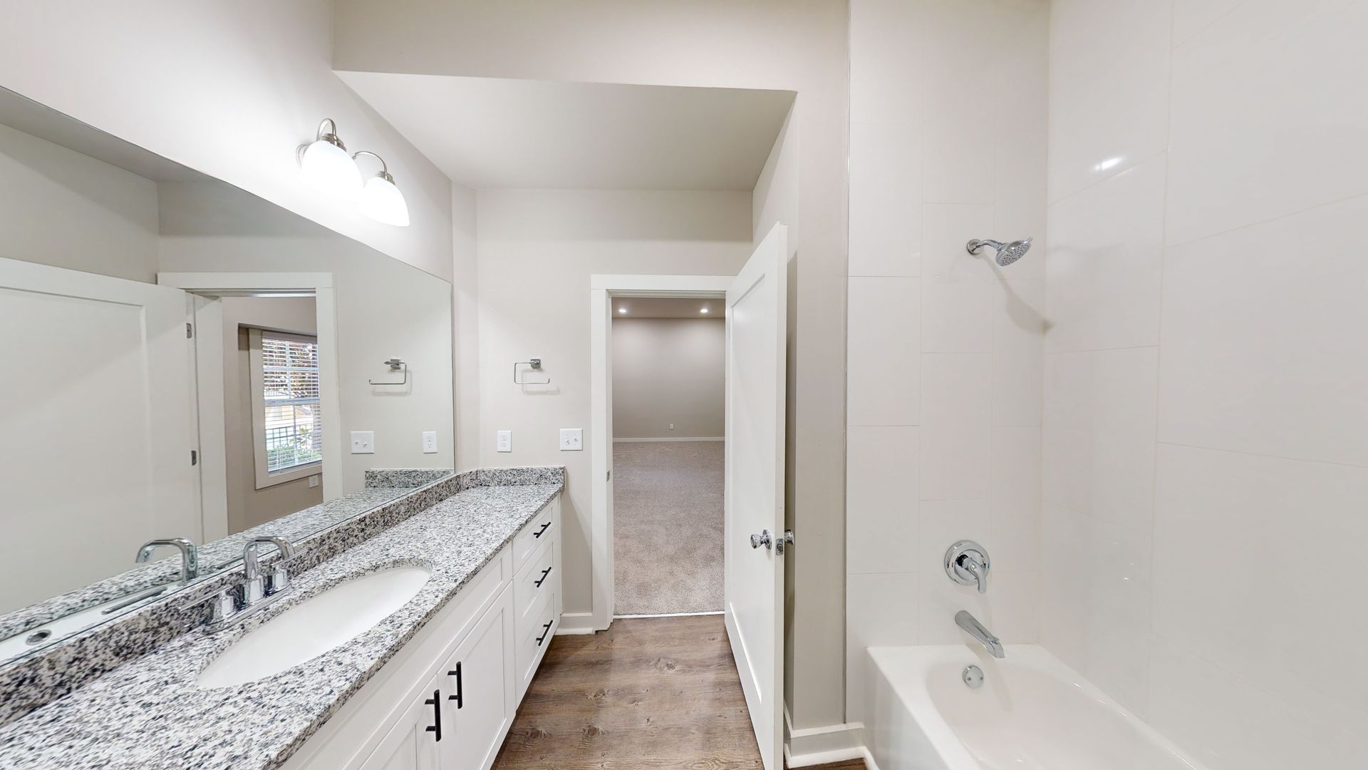 Bright bathroom with double vanity, large mirror, and bathtub in a clean white interior.