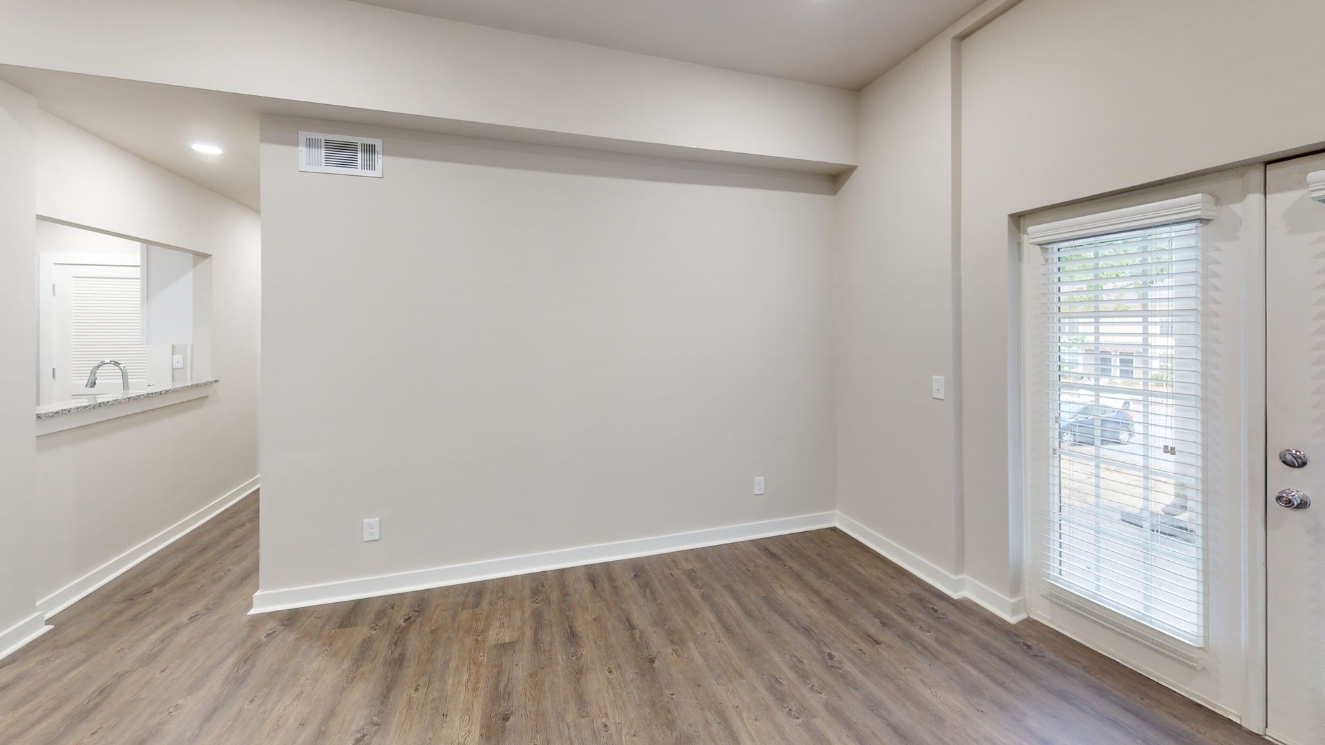 Empty modern living room with gray walls, wood floor, mirrored wall, and sliding glass door with blinds