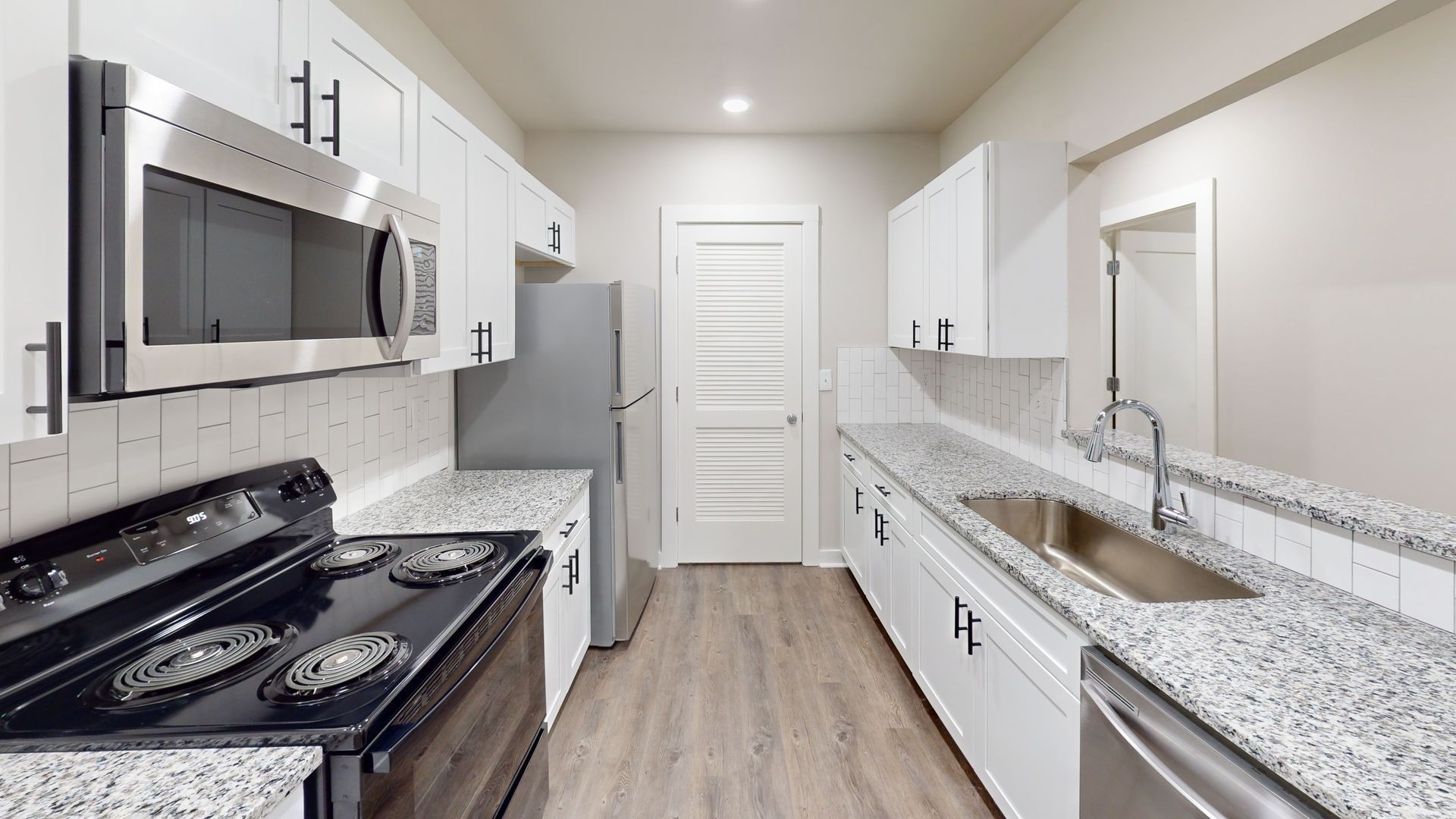 Bright modern kitchen with white cabinets, stainless appliances, granite counters, and wood-look flooring