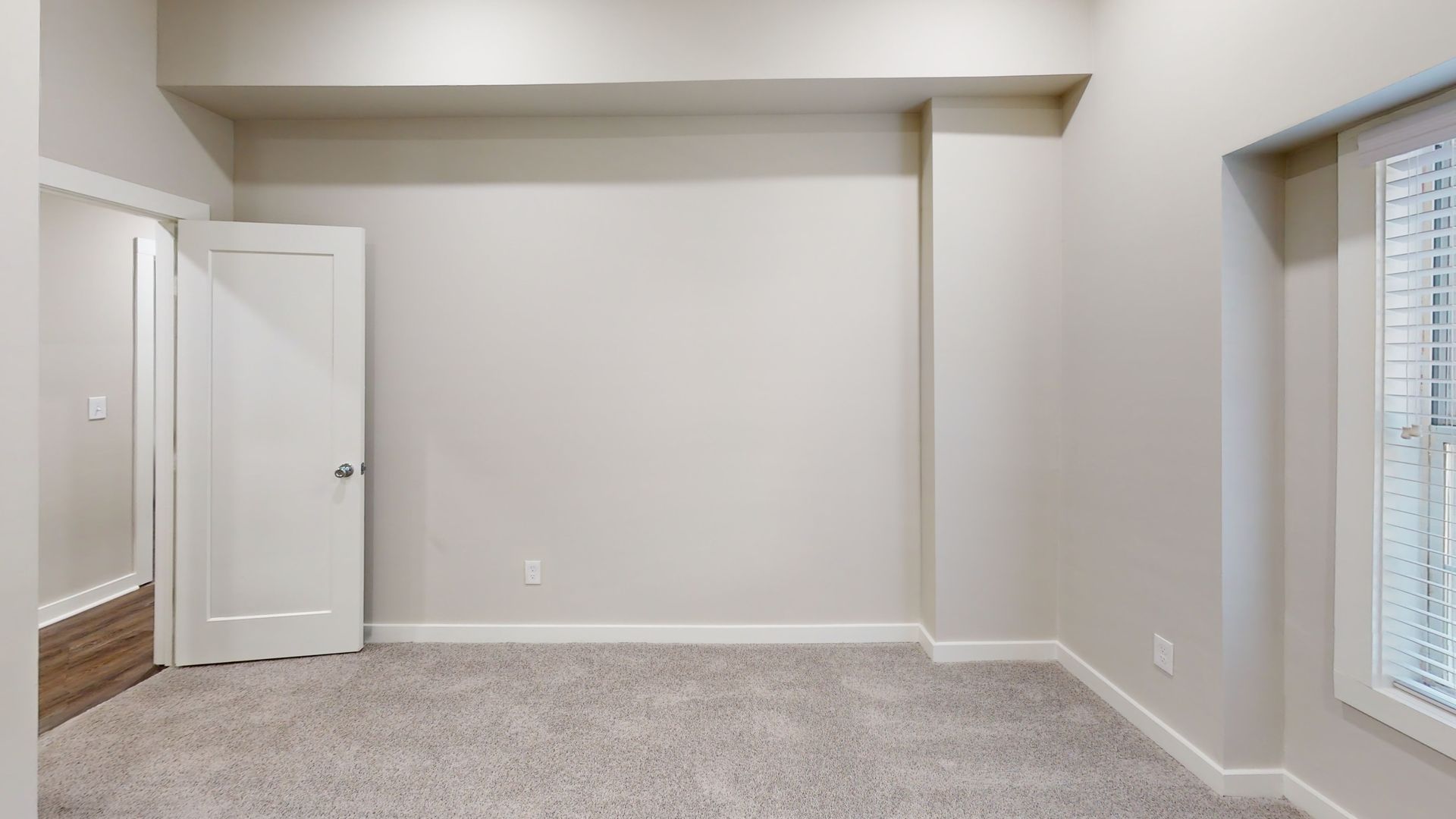 Empty beige room with carpet, white trim, and a window on the right.