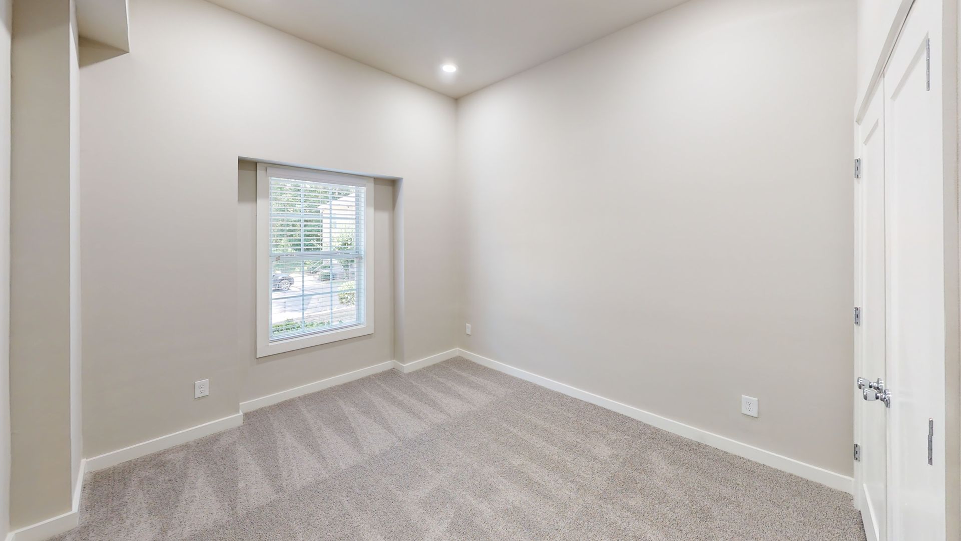 Empty beige bedroom with gray carpet, white trim, a window, and recessed ceiling light