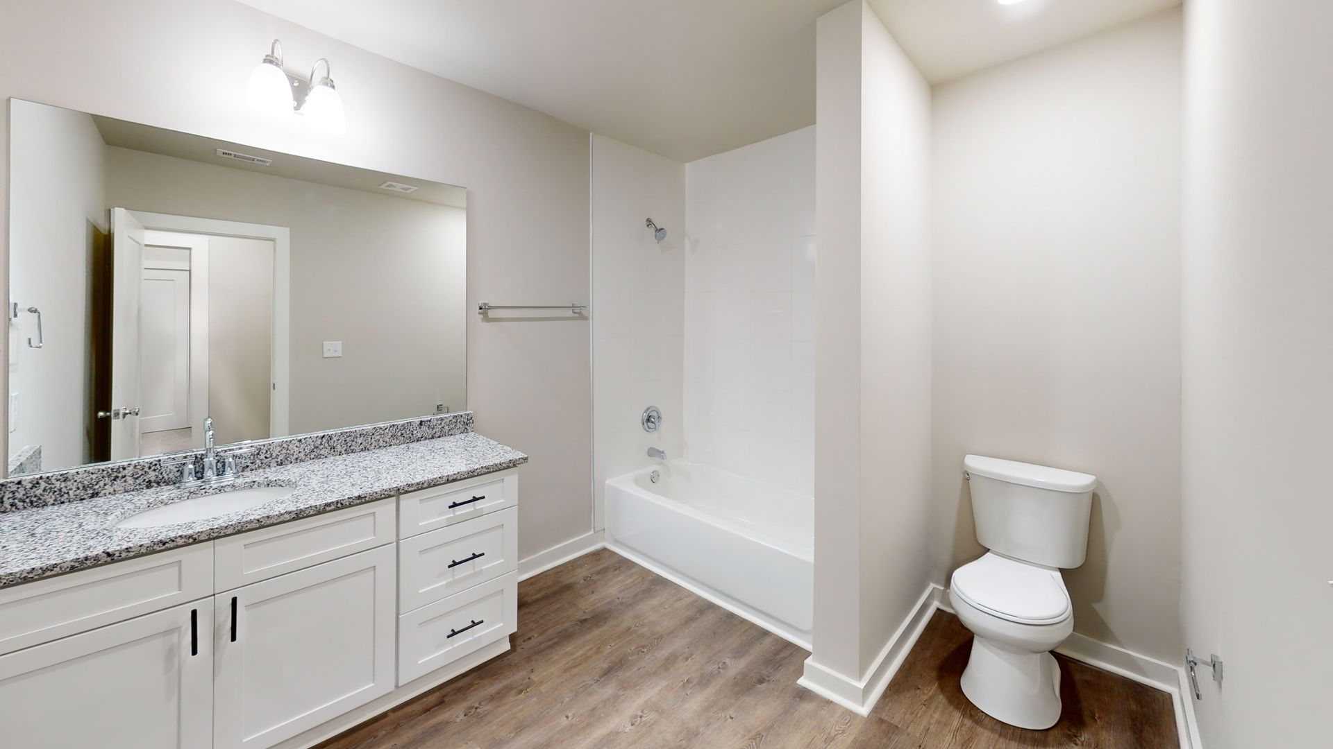 Modern bathroom with white vanity, large mirror, tub shower, and toilet on wood-look flooring