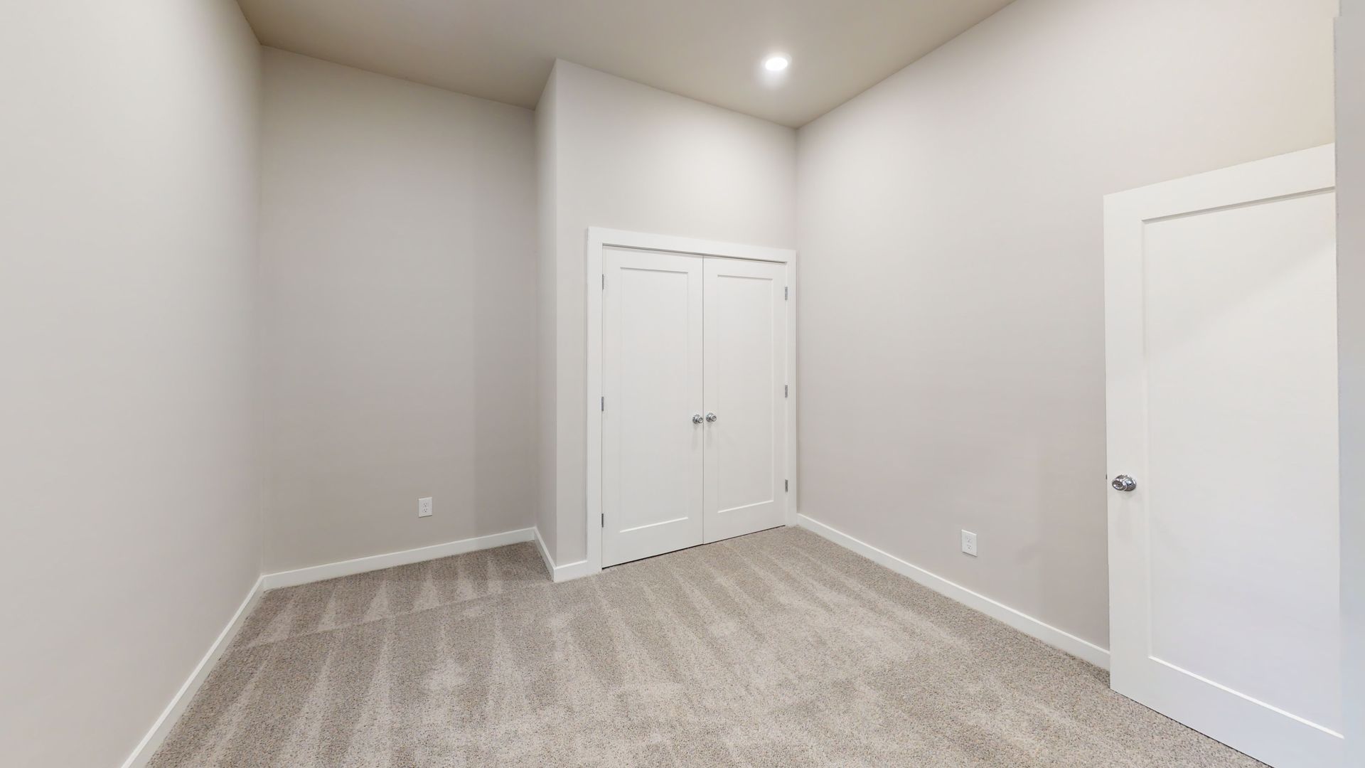 Empty beige room with carpet, white trim, and two white doors under recessed ceiling lights