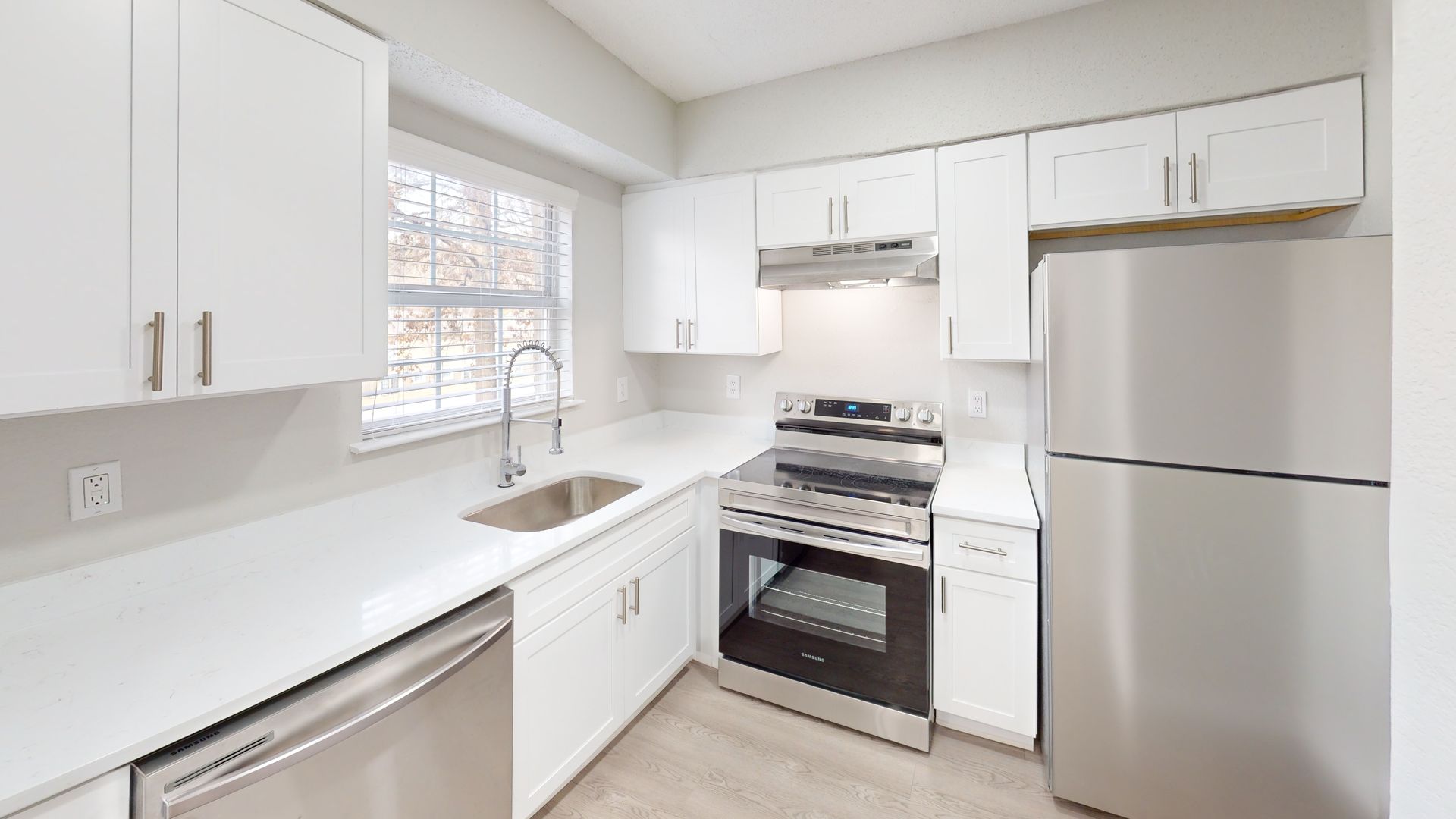 Bright white kitchen with stainless steel appliances, window over the sink, and light countertops.