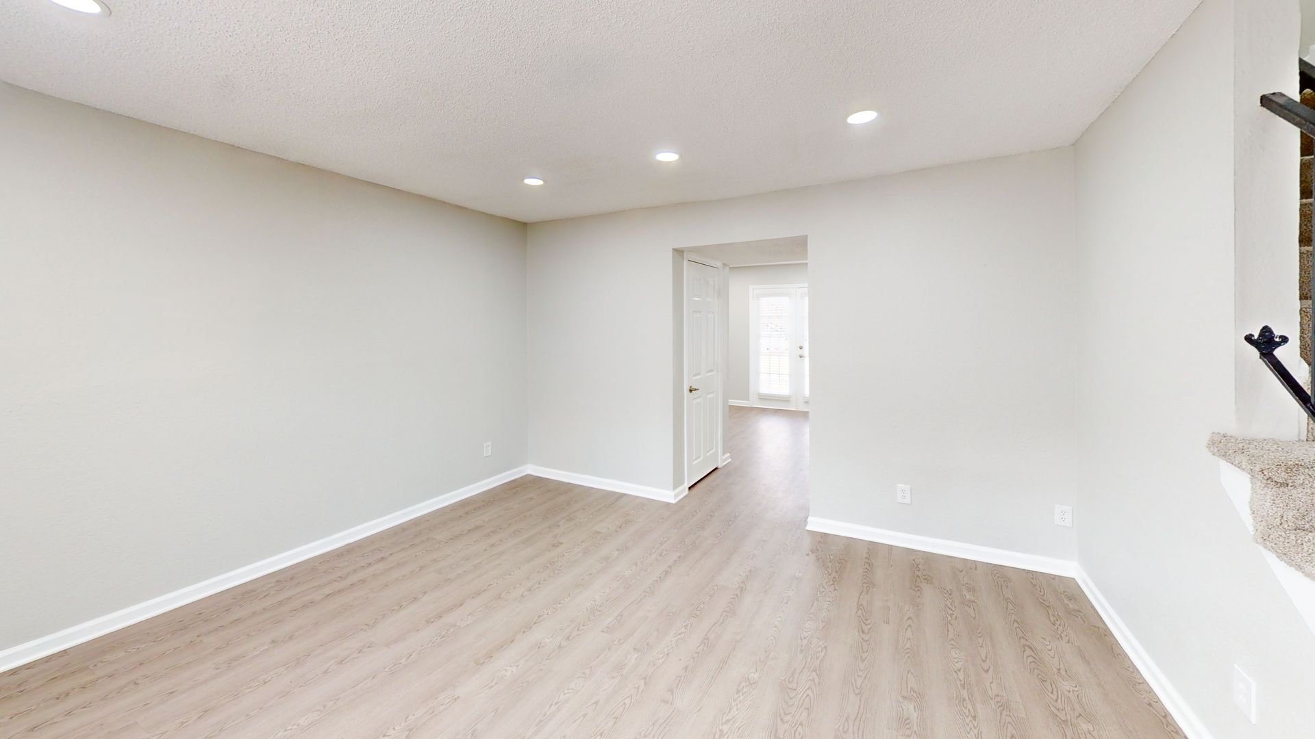 Empty bright room with light wood floors, white walls, recessed lights, and an open doorway.