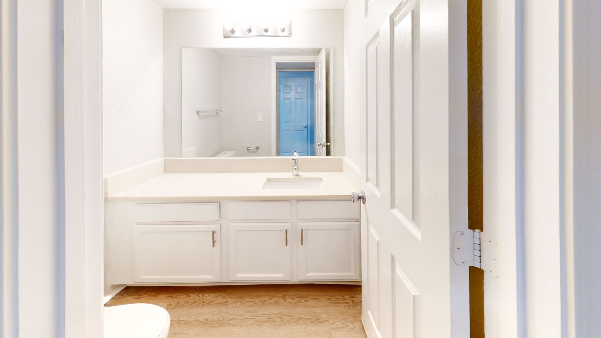 Bright white bathroom vanity with double sink, mirror, and open doorway to a blue-tinted room.