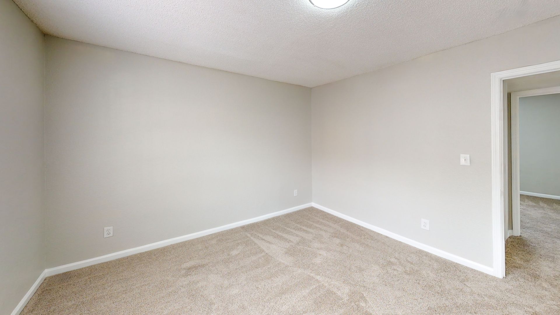 Empty beige carpeted bedroom with light gray walls and an open doorway.