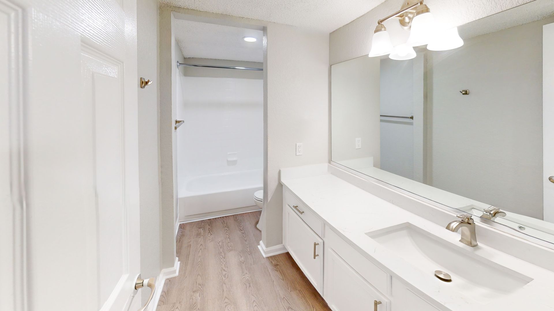 Bright bathroom vanity with large mirror, white cabinets, and an open closet in the background