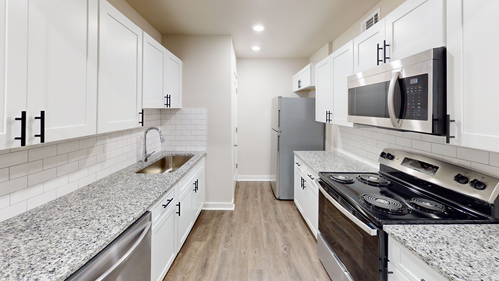 Bright modern kitchen with white cabinets, granite counters, stainless appliances, and wood-style flooring