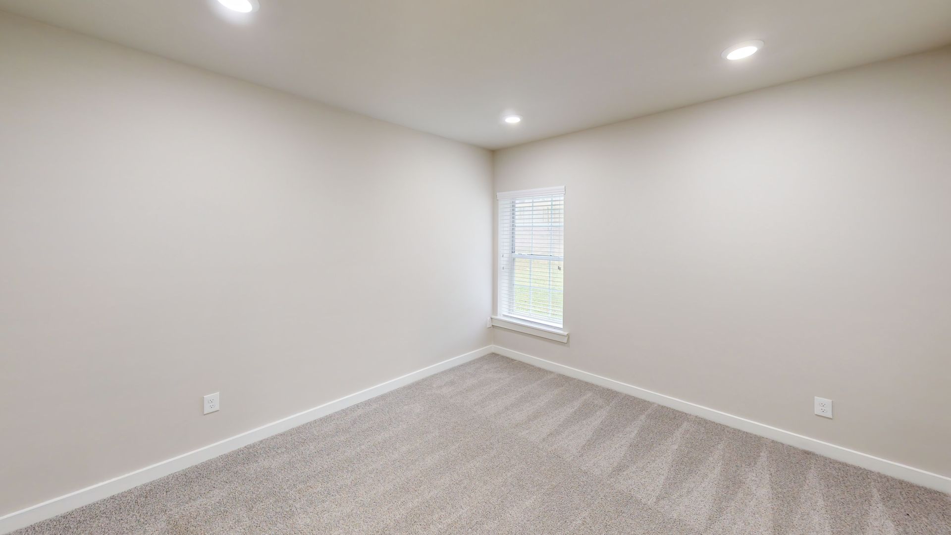 Empty beige bedroom with carpet, white walls, recessed lights, and a small window.