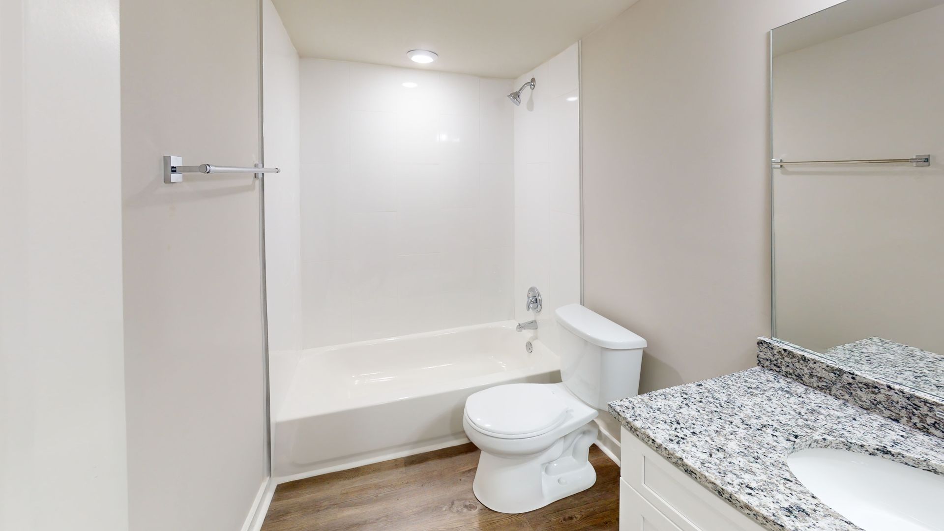 Small beige bathroom with a tub, toilet, towel bars, and granite vanity counter