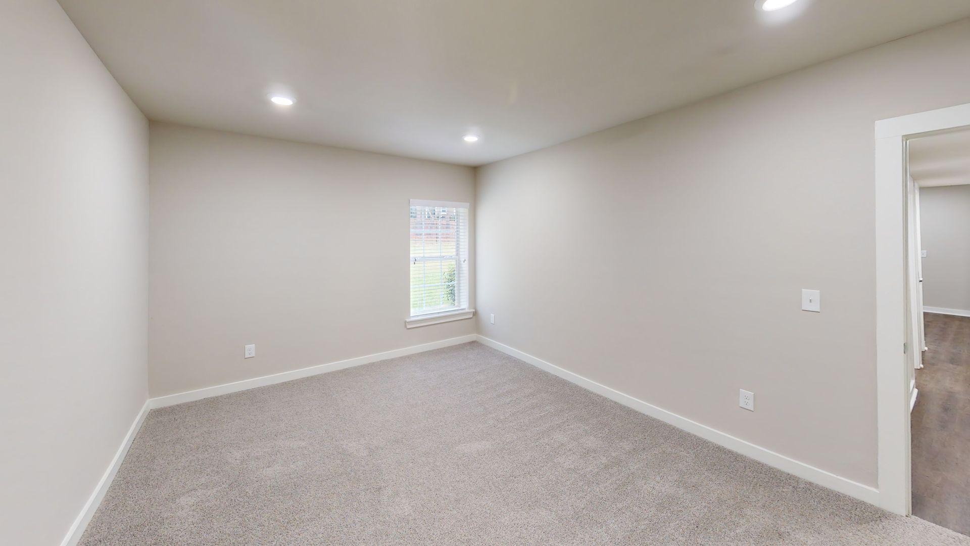Empty beige carpeted bedroom with white walls and a small window.