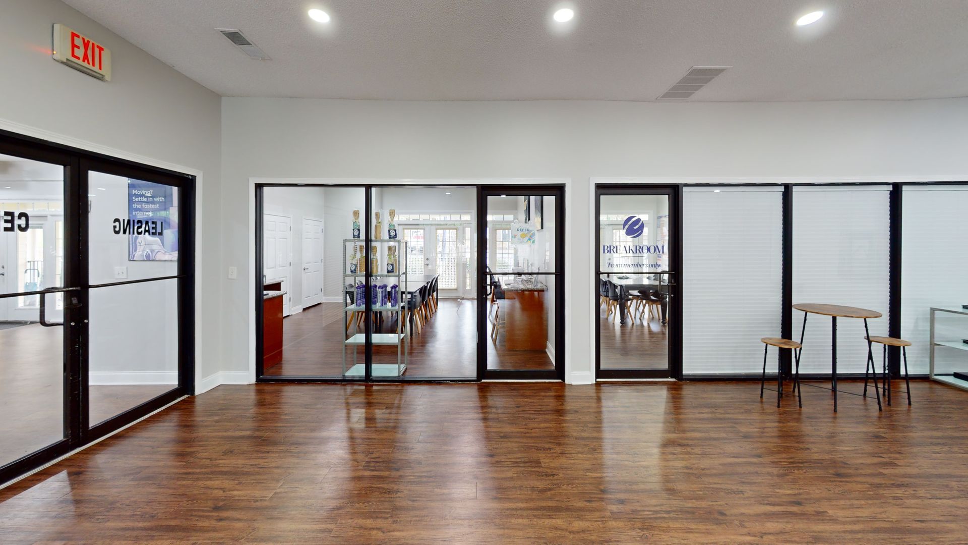 Empty modern studio with wood floors, glass doors, tables, and bright overhead lights