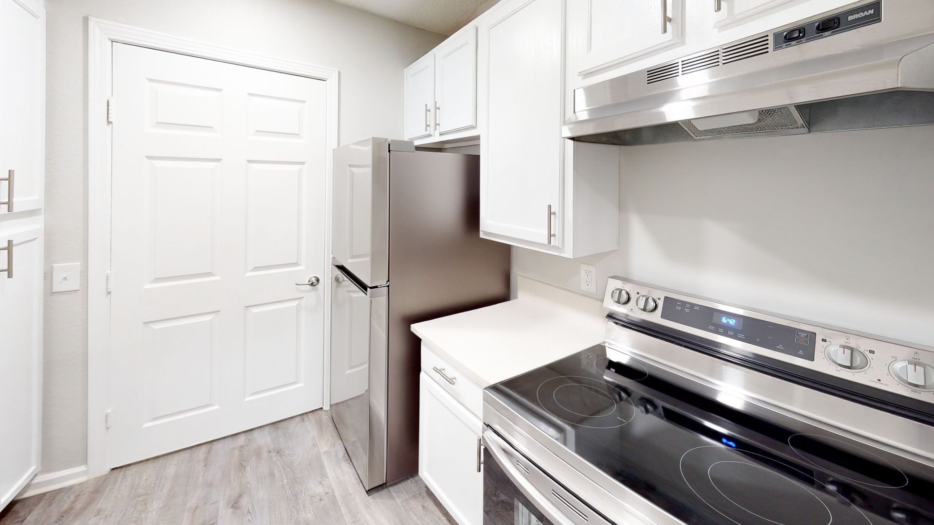 Bright kitchen with white cabinets, stainless steel appliances, and a white door by a refrigerator