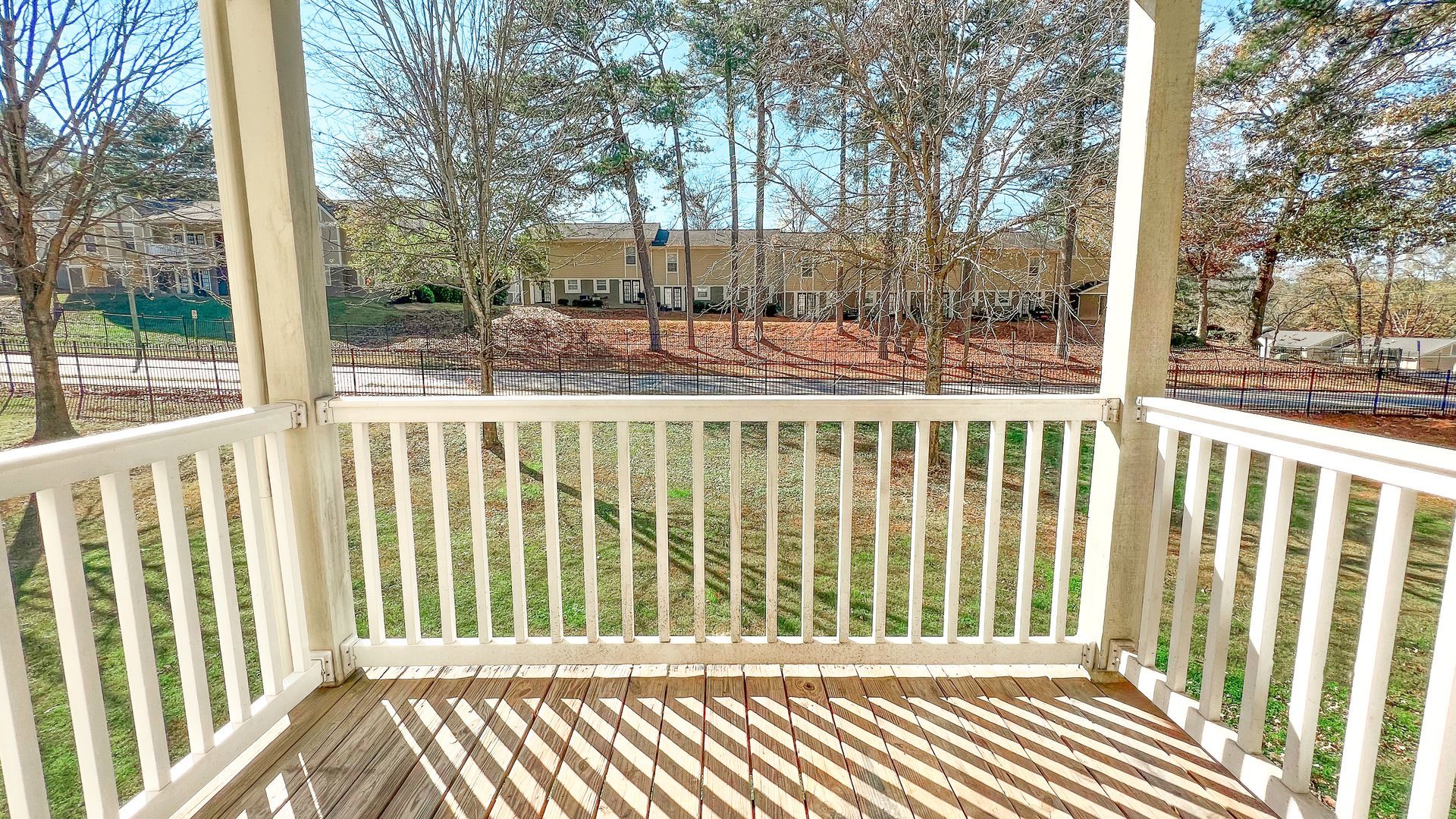 White porch overlooking a grassy yard and leafless trees in bright daylight