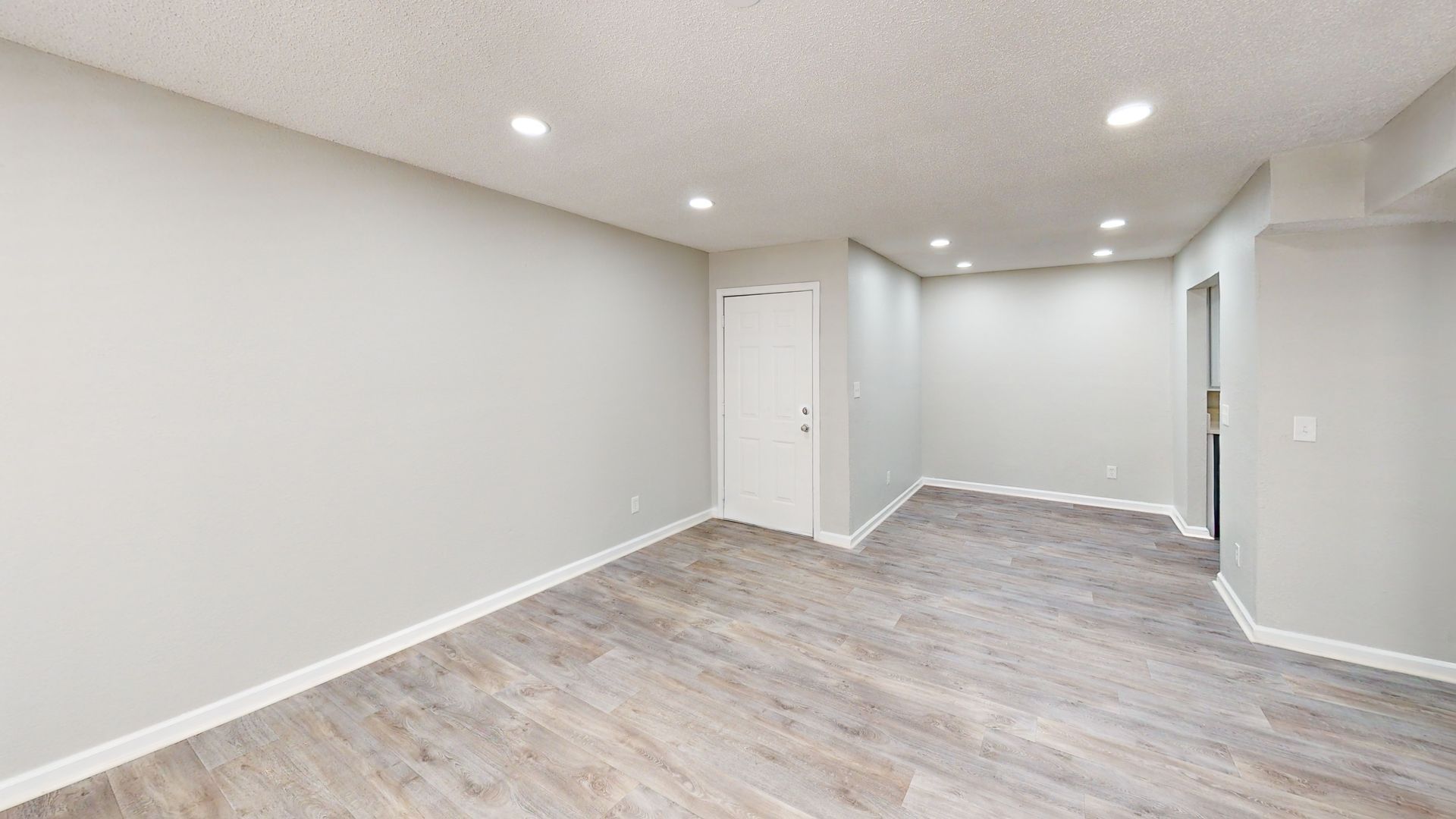 Empty modern basement room with gray walls, white trim, recessed lights, and wood-look flooring