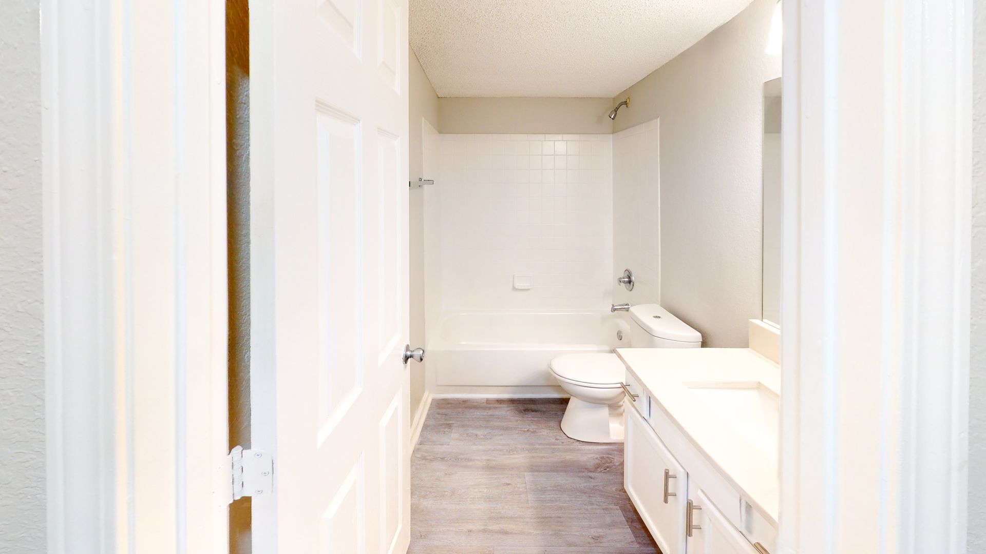 Bright white bathroom with bathtub, toilet, and vanity in a narrow hallway view