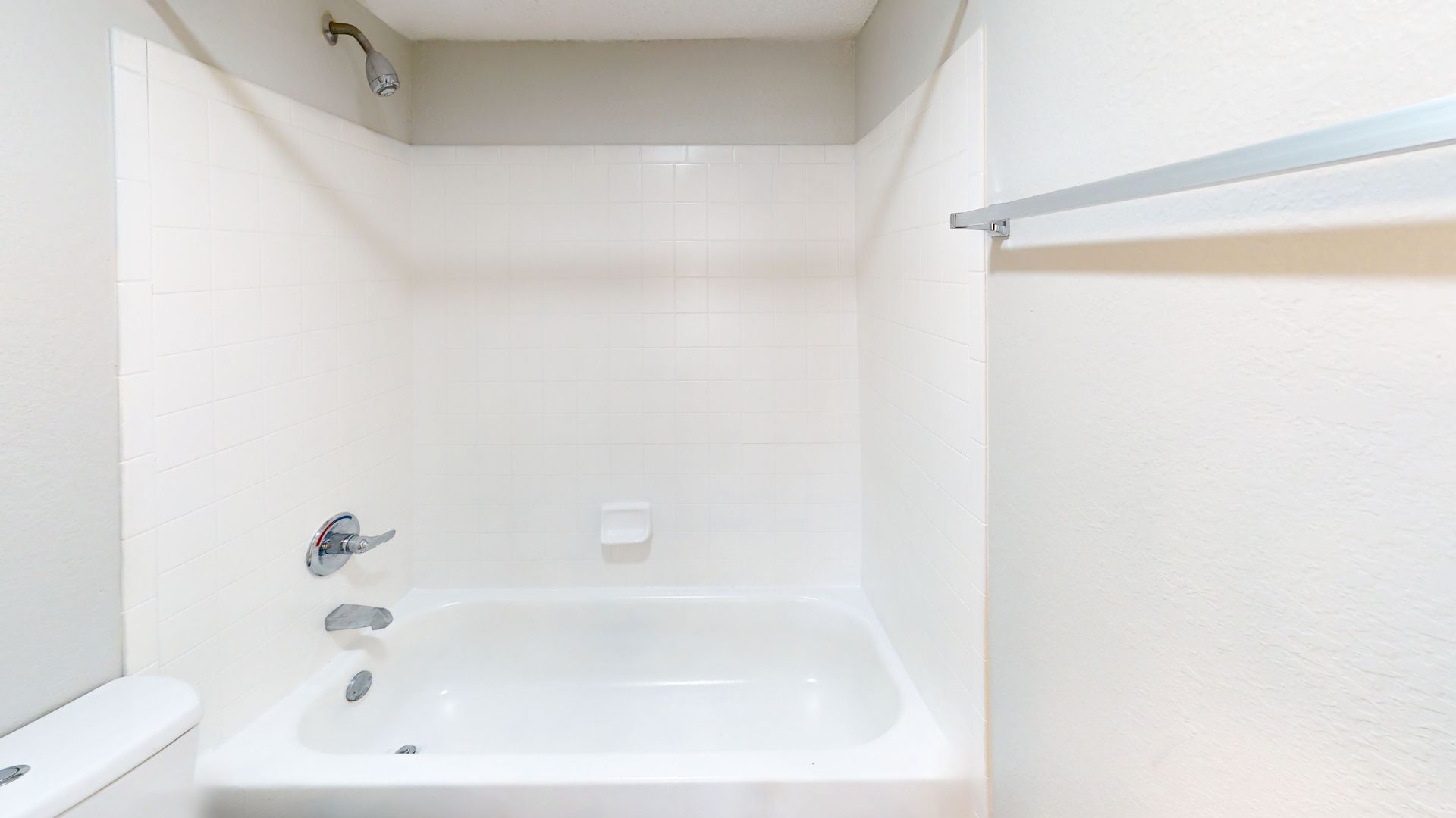 Empty white bathroom with a bathtub and shower fixture, plus a towel shelf on the right