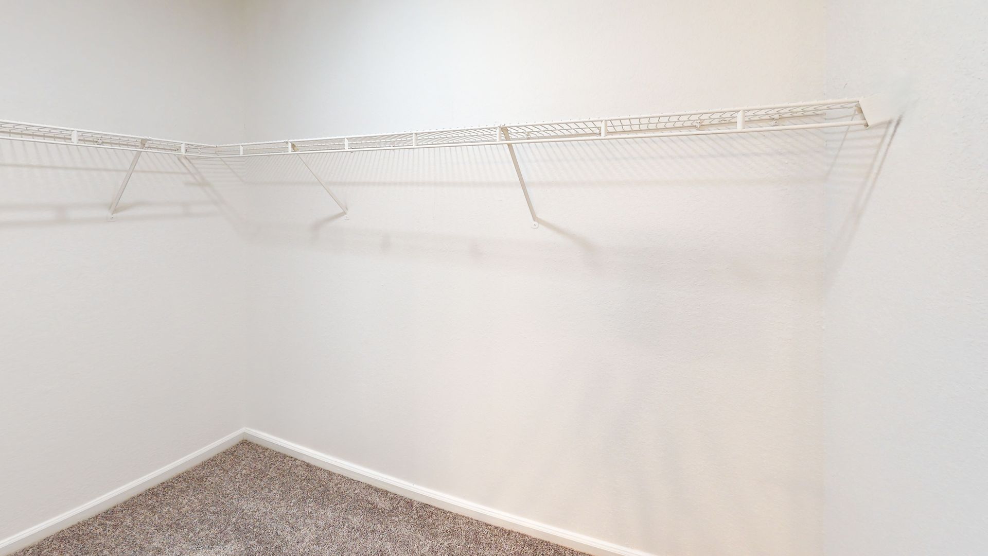 Empty white closet corner with a wire shelf and carpeted floor