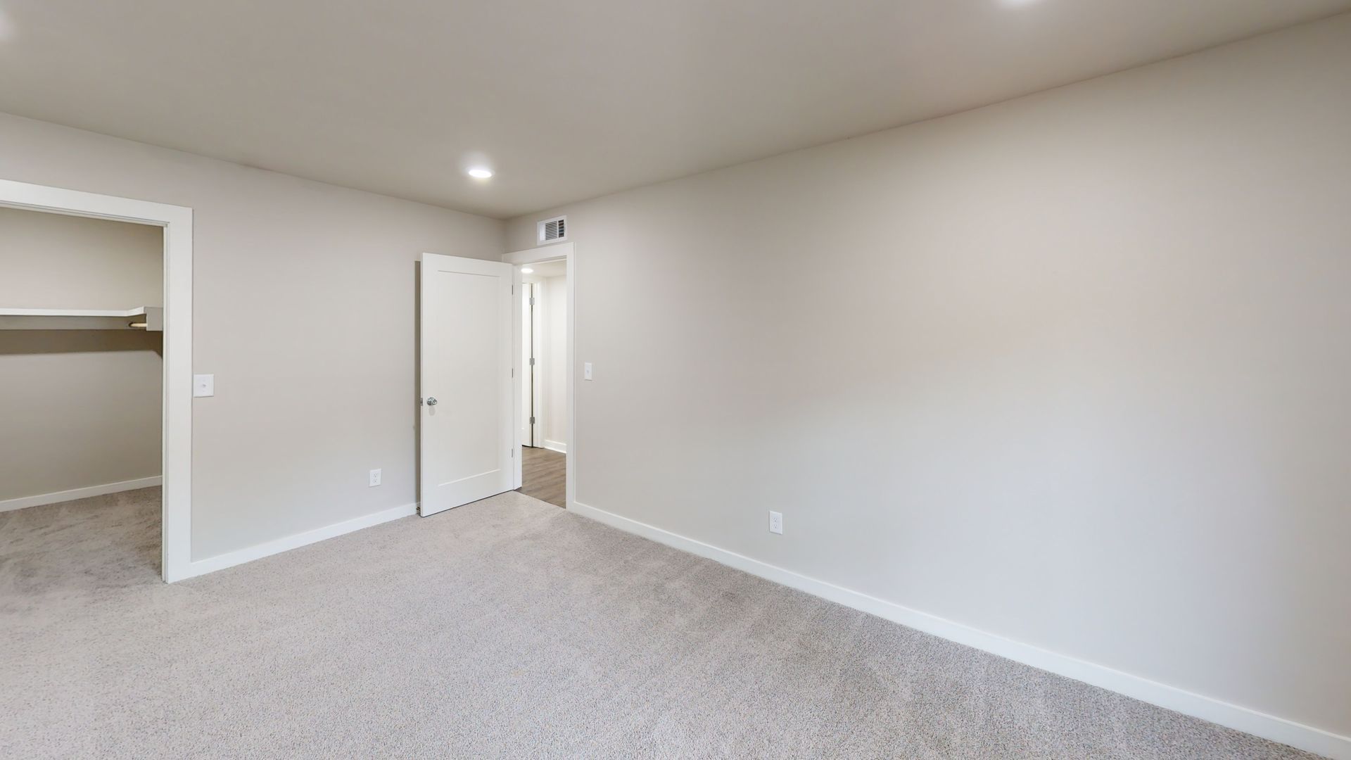 Empty beige bedroom with carpet, open closet, and an open door to a hallway