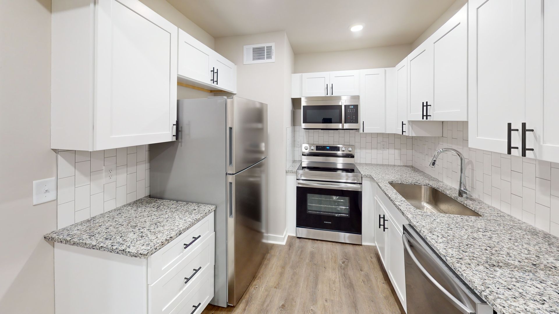 Bright white galley kitchen with granite counters, stainless appliances, and wood-look flooring.