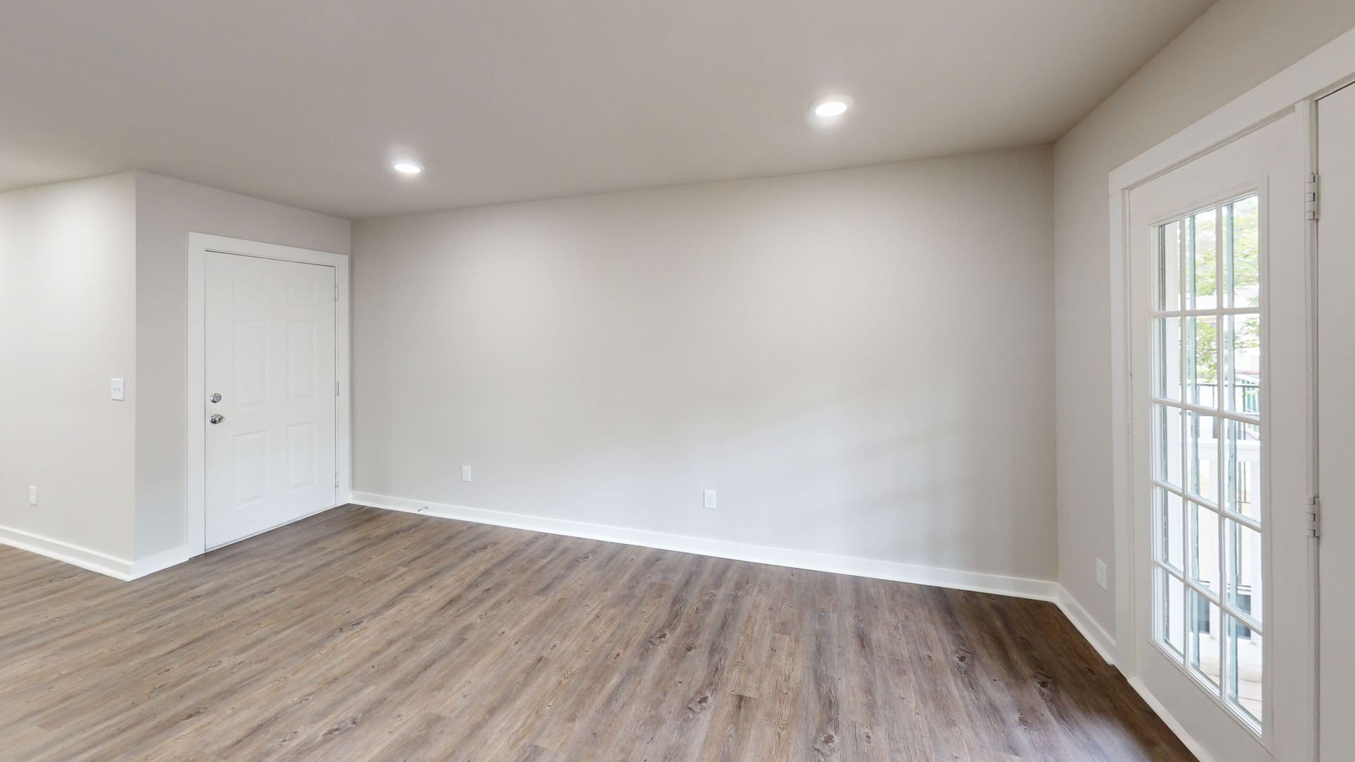 Empty modern living room with light gray walls, wood floors, recessed lights, and French doors