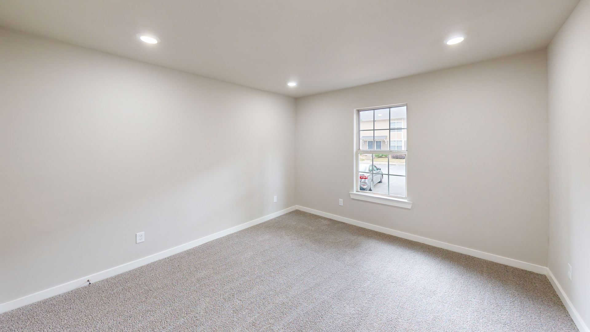 Empty beige bedroom with carpeted floor, white walls, and a single window letting in daylight