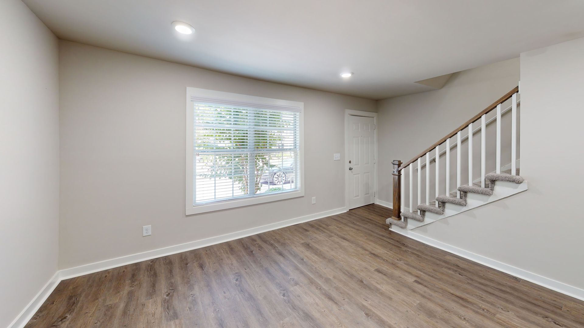 Empty living room with gray walls, wood flooring, a large window, and stairs on the right