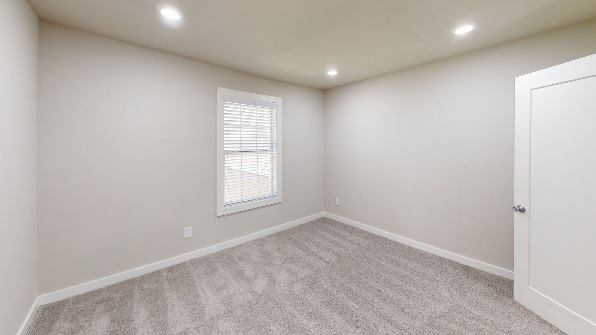 Empty beige bedroom with carpet, recessed lights, a window, and a white closet door.