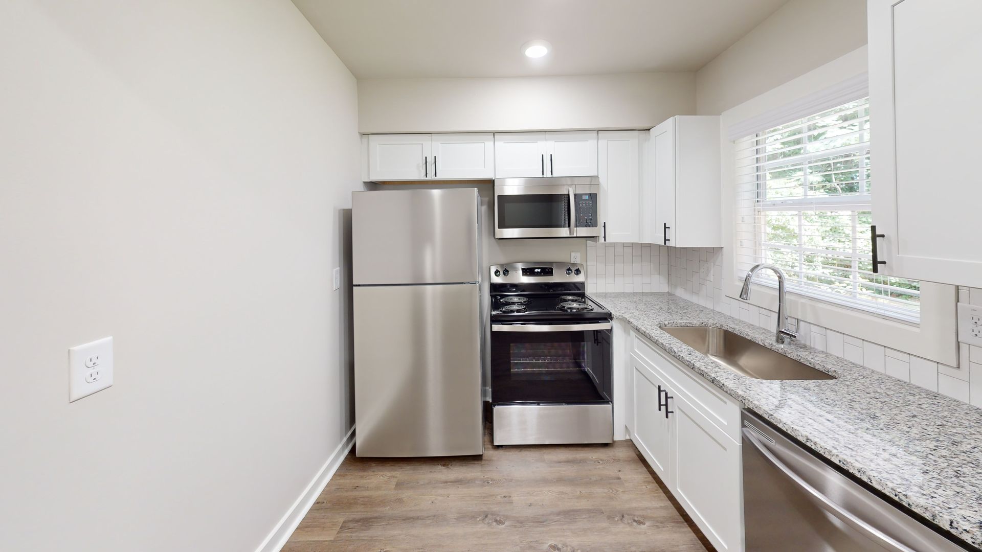 Bright modern kitchen with stainless steel appliances, white cabinets, and a window over the sink.