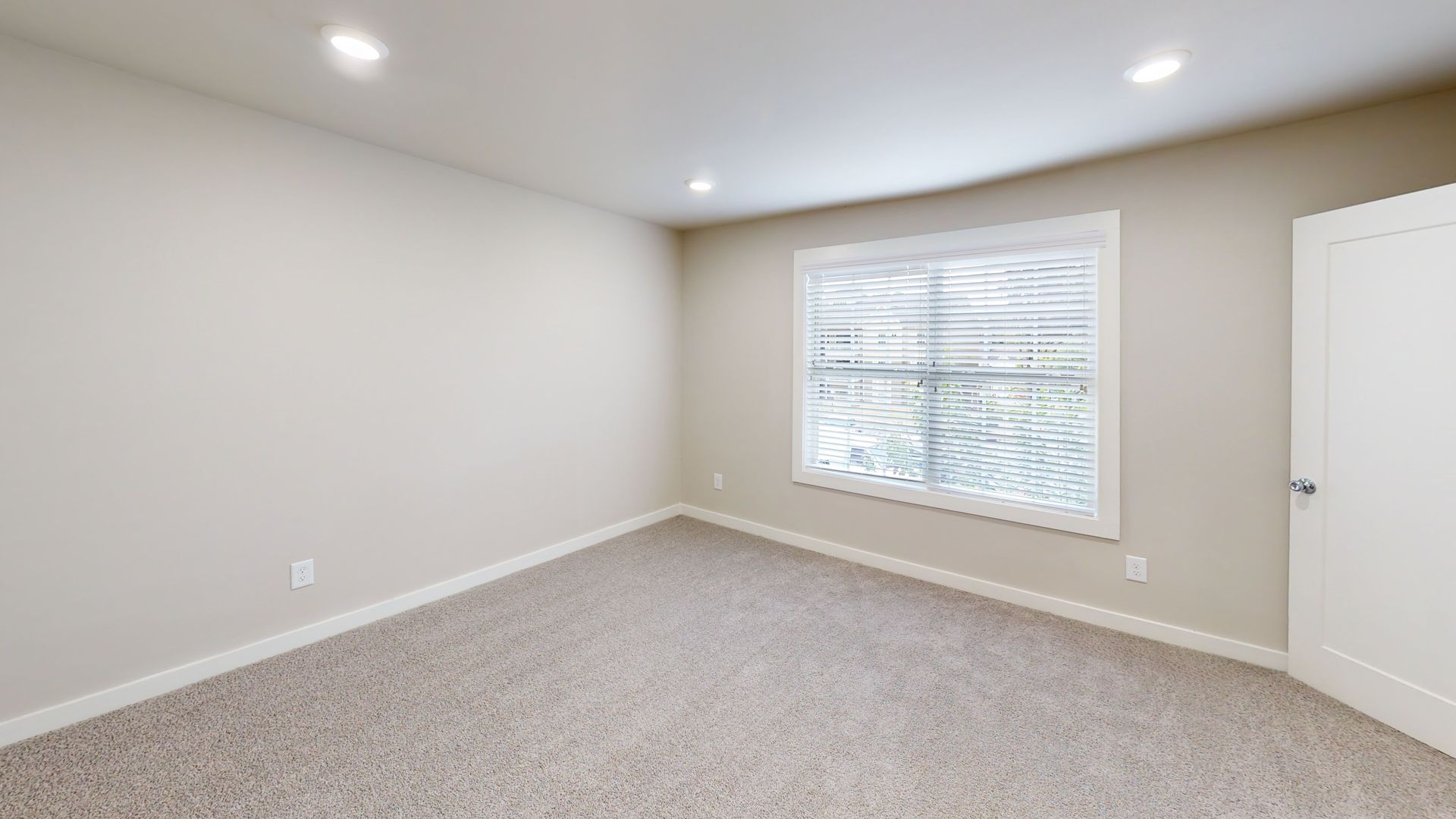 Empty beige bedroom with carpet, window, recessed lights, and a white closet door