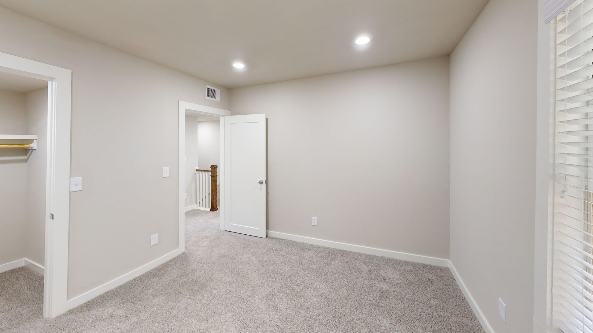 Empty beige bedroom with carpet, recessed lights, open closet, and white blinds.