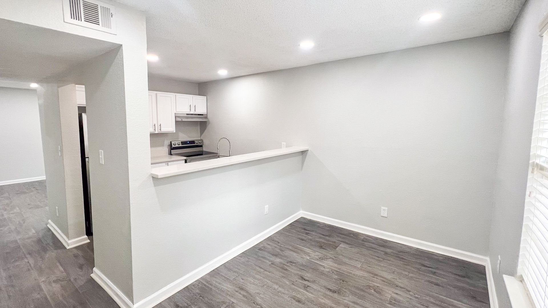 Empty modern room with gray walls, carpeted floor, and a small kitchen pass-through counter