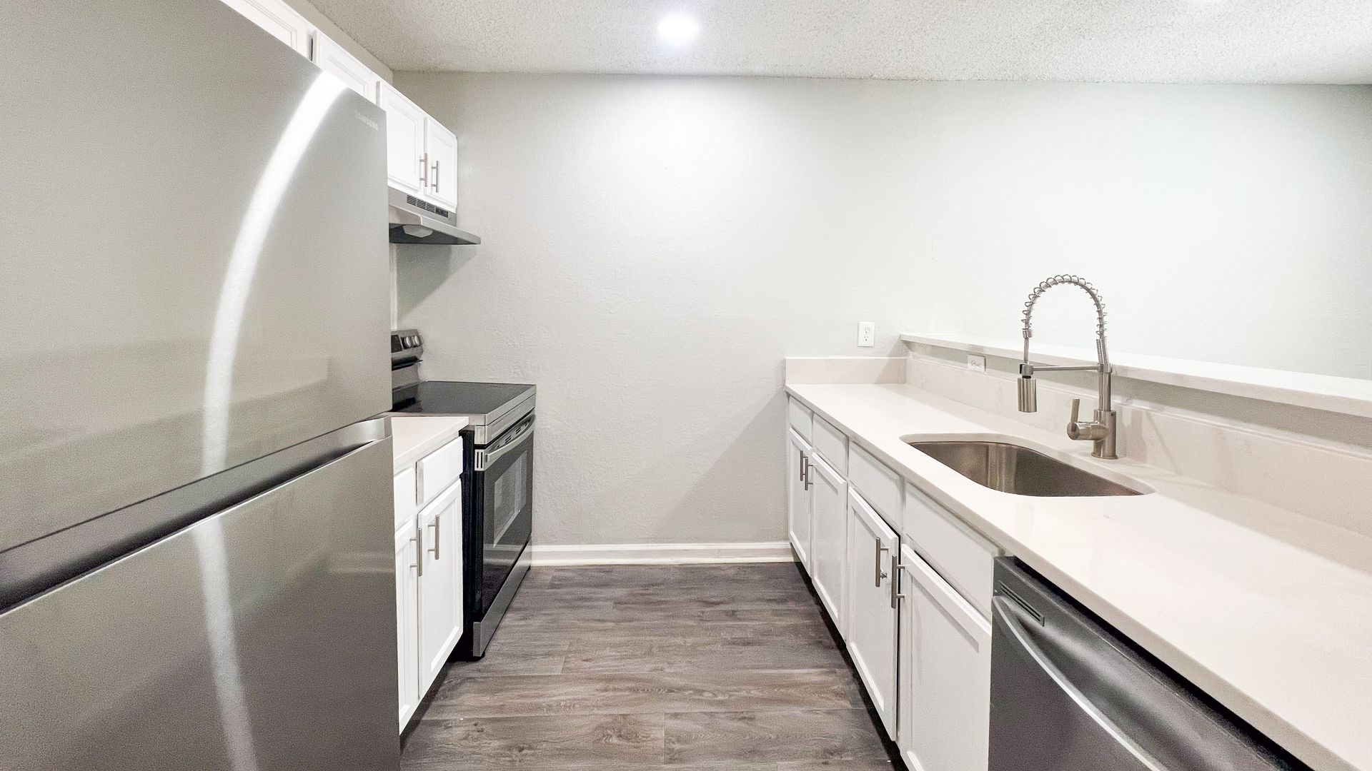 Modern galley kitchen with white cabinets, stainless steel appliances, and dark wood flooring