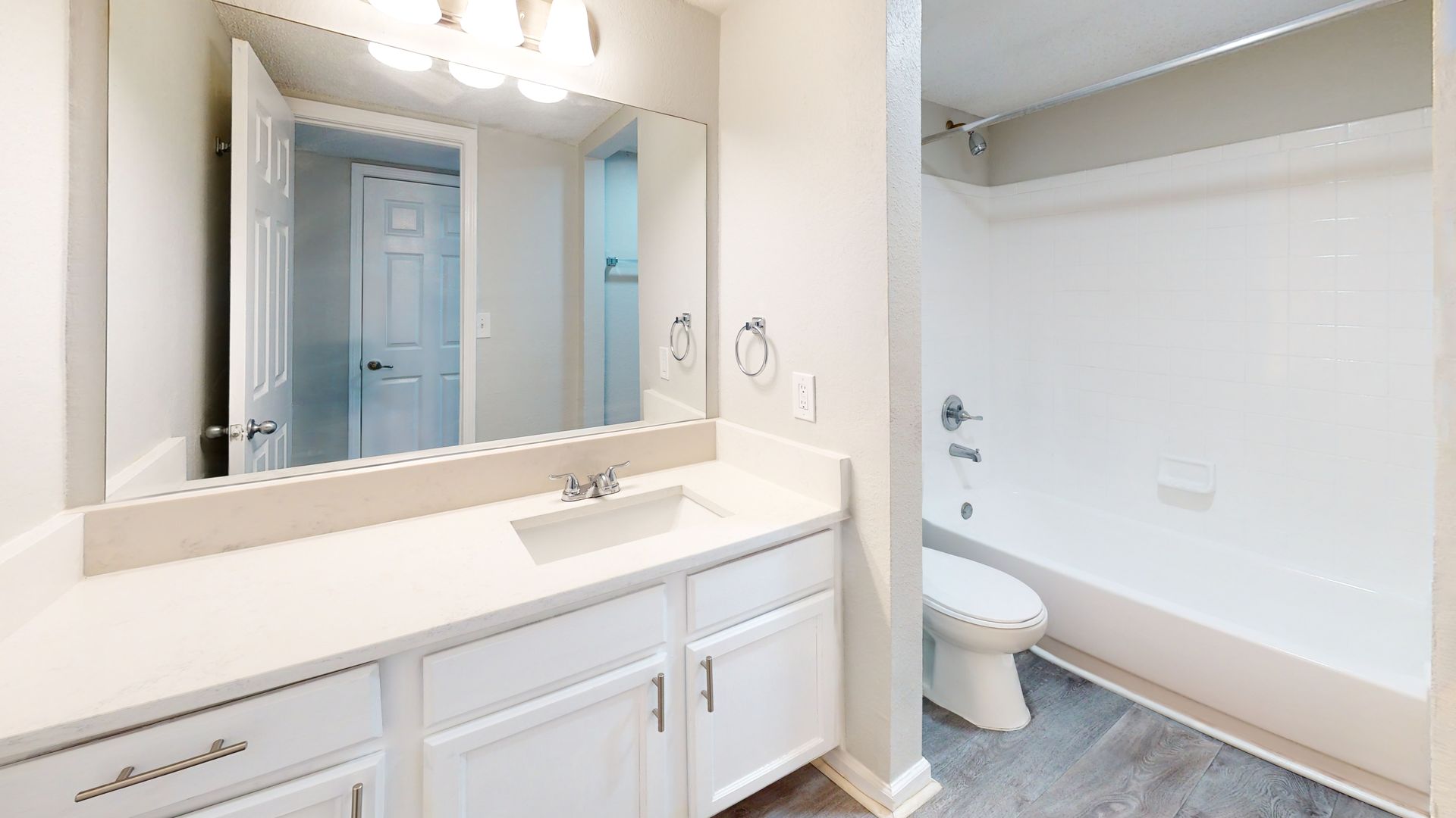 Bright white bathroom vanity with large mirror, sink, toilet, and gray floor tiles
