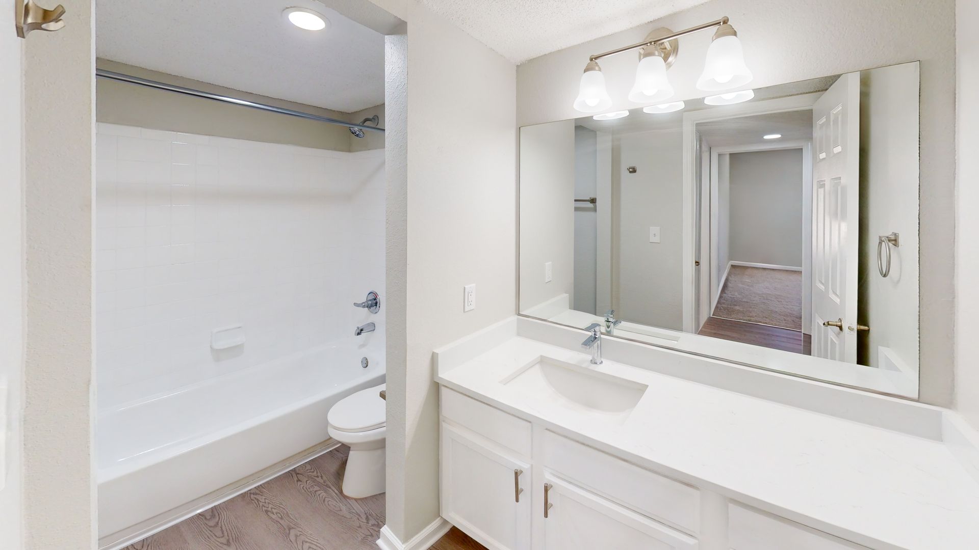 Bright bathroom vanity with large mirror, sink, and adjacent shower-tub with toilet visible
