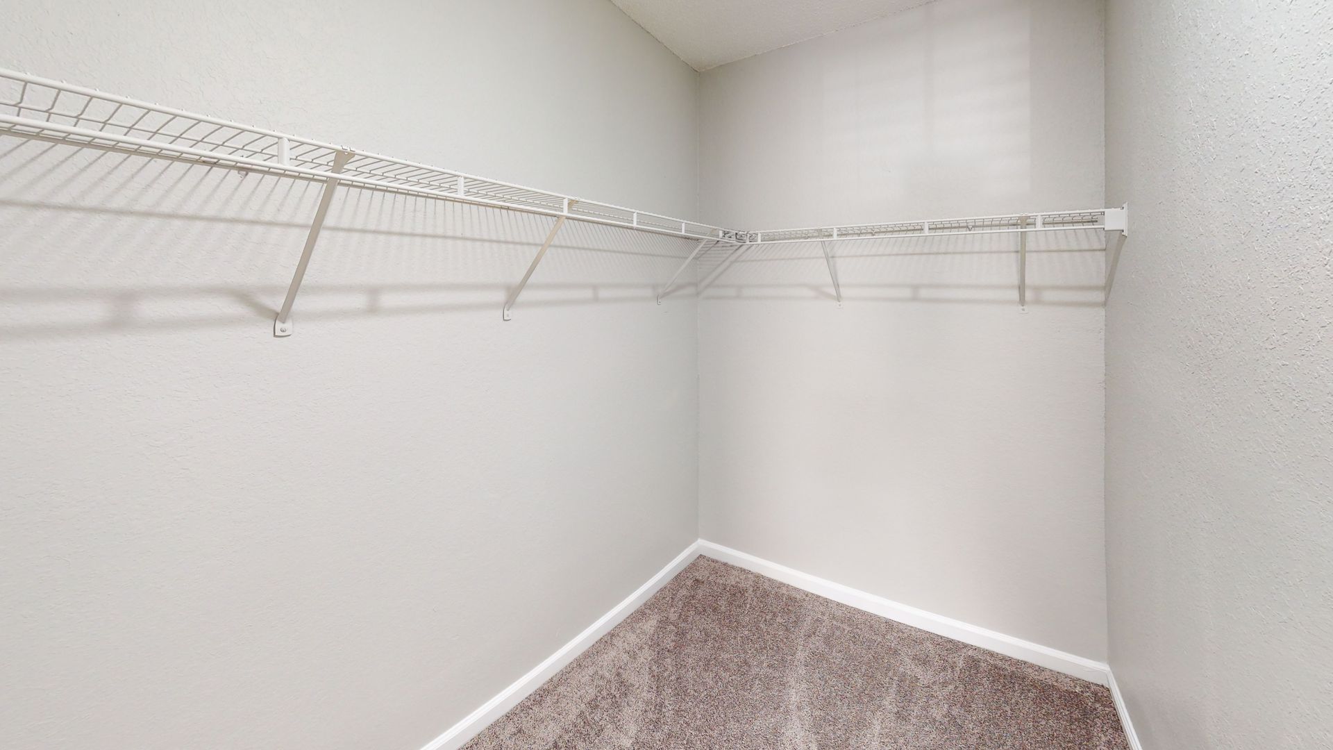 Empty carpeted closet with white walls and wire shelving on two sides
