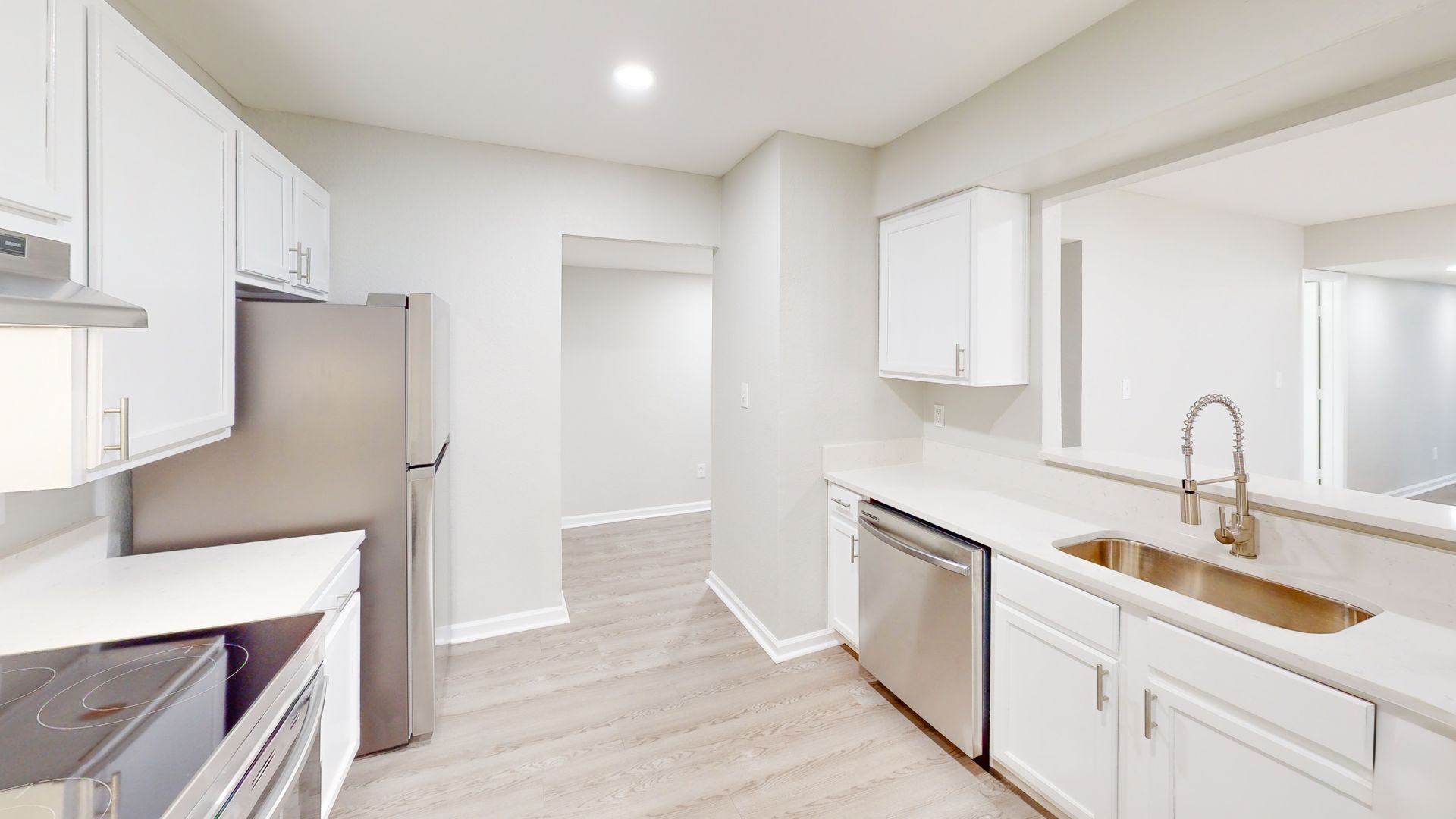 Bright modern kitchen with white cabinets, stainless appliances, and light wood floors