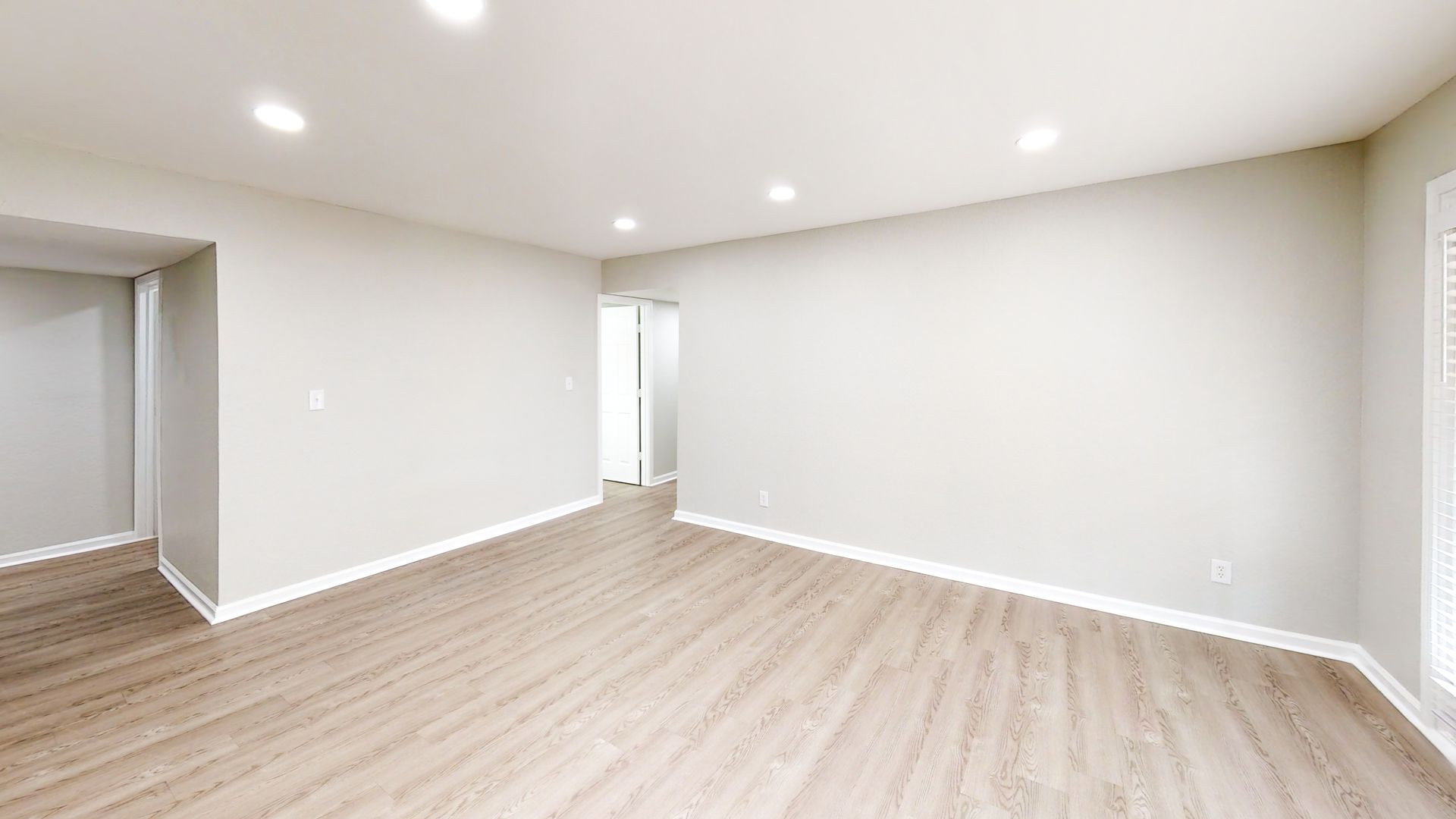 Empty modern living room with white walls, light wood floors, and recessed ceiling lights