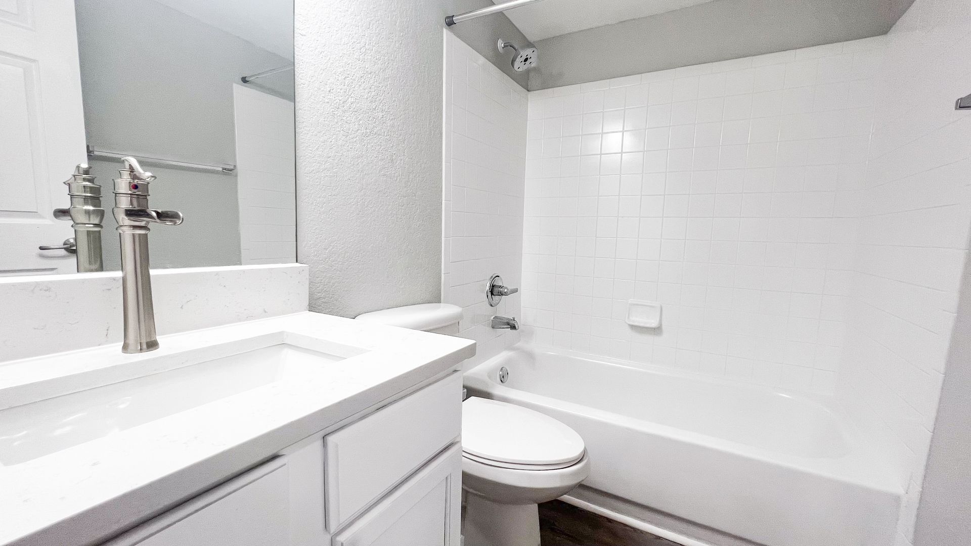 Bright bathroom with white vanity, sink, toilet, and bathtub against tiled walls