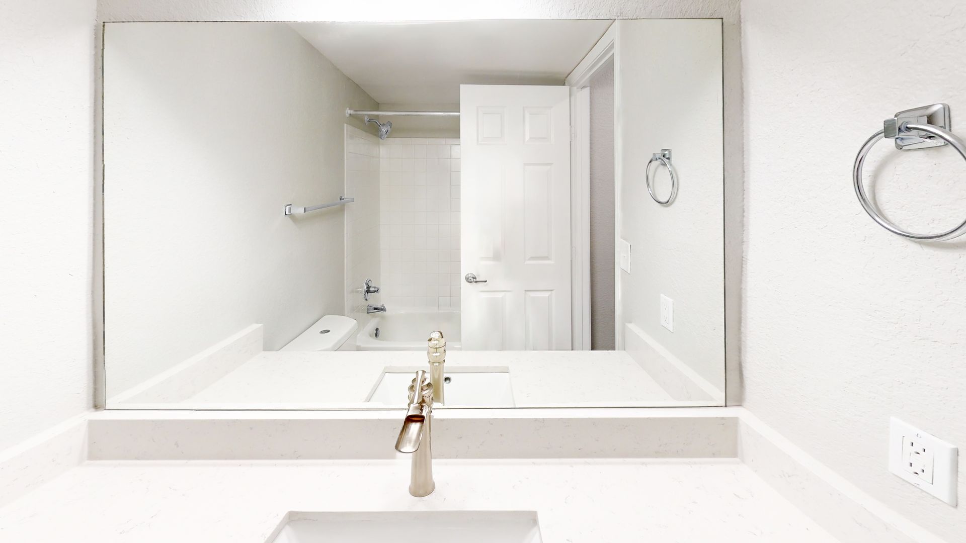 Bright white bathroom vanity with large mirror, sink faucet, towel rings, and shower in the background