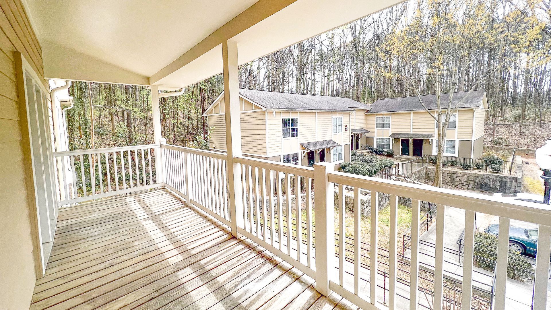 Covered apartment balcony with white railing overlooking a wooded residential courtyard