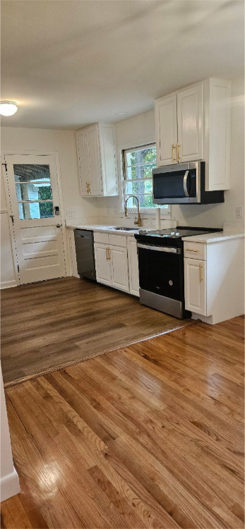 Empty room with hardwood floors, white walls, a fireplace, and large windows.