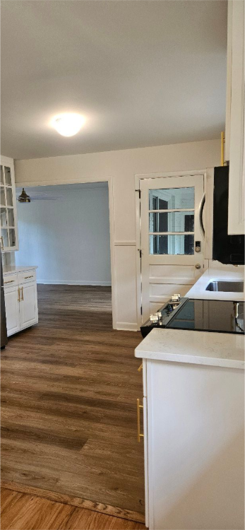 Empty kitchen and dining area with white walls, wood floor, and a window at the far end.