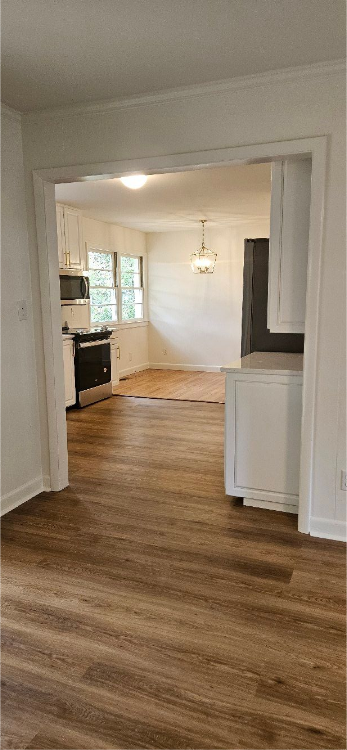Empty hallway with white trim, wood floors, and a bright window at the far end.
