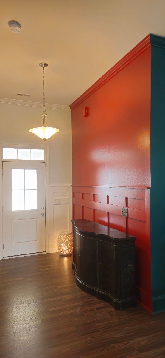 An entryway with a red wall, dark cabinet, and white door.