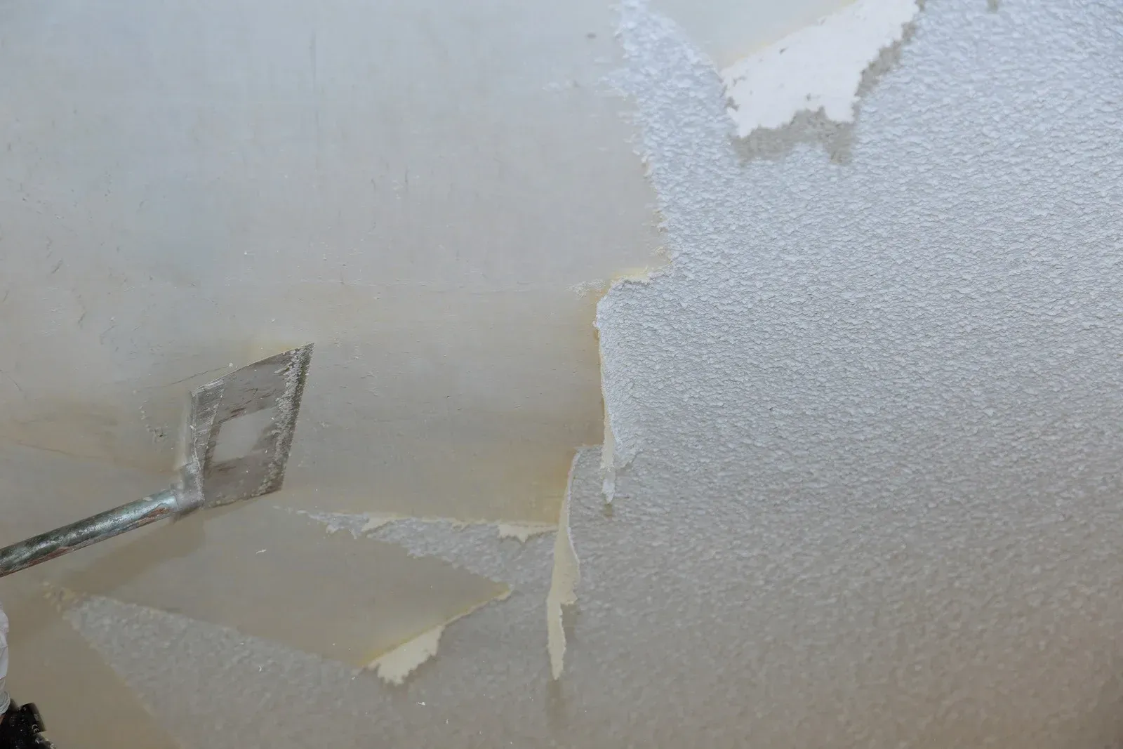 A man is standing on a ladder painting a ceiling.