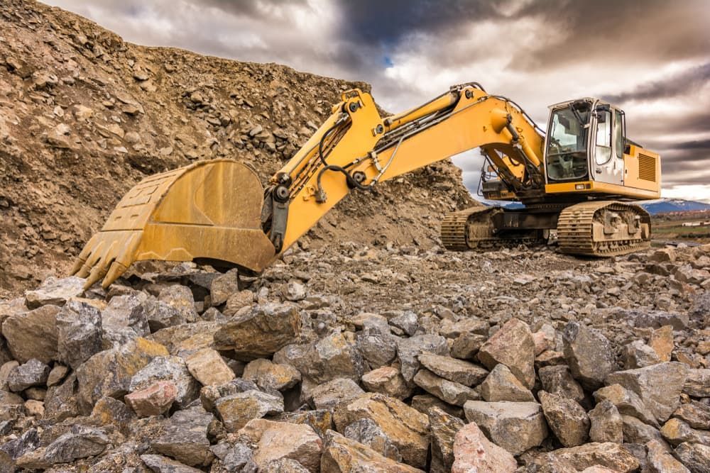 A Yellow Excavator is Working on a Pile of Rocks in a Quarry — Andrew Johnston Haulage In Grafton, NSW
